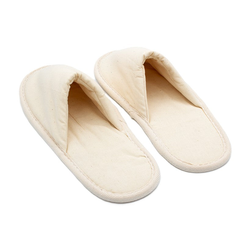 Pair of simple beige fabric slippers with closed toes, placed side by side on a white background