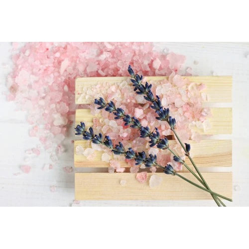 Lavender sprigs on wooden tray with scattered pink bath salts on a white surface