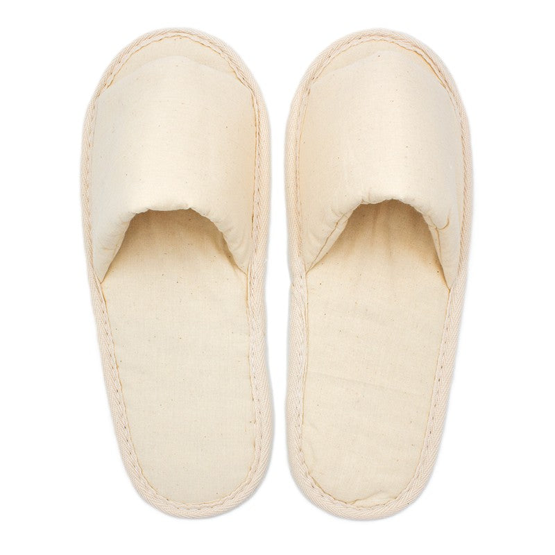 Pair of plain beige fabric slippers with closed toes, simple design, viewed from above on a white background.