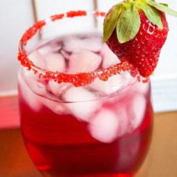 Glass of red iced drink with sugared rim, garnished with a fresh strawberry, served over ice cubes