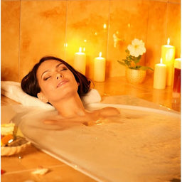 Relaxed woman enjoying a bubble bath in candlelit bathroom with warm lighting and floral decor