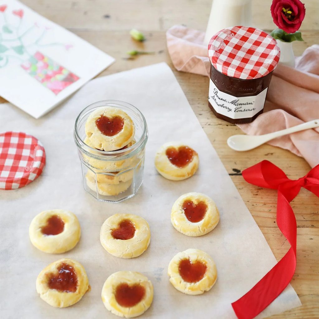 Heart-shaped cookies with strawberry jam centers arranged on a white plate for Valentine’s Day