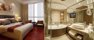 Luxurious hotel room with a large bed, warm decor, and an adjoining modern bathroom featuring a spa tub and vanity.