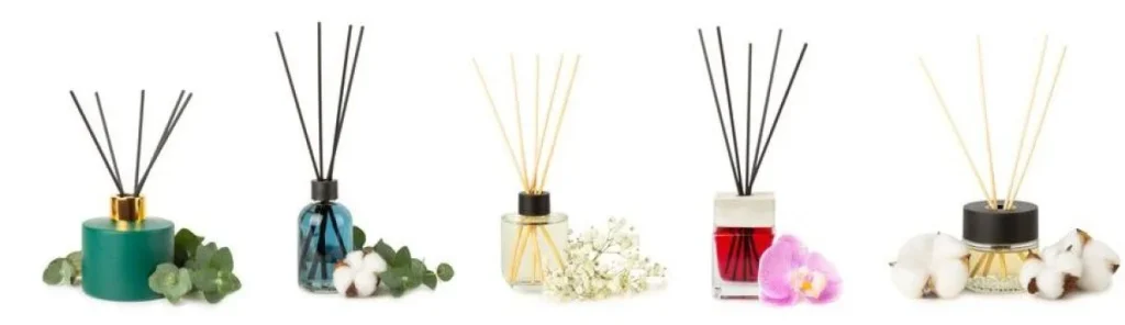 Five assorted reed diffusers in decorative bottles with floral accents placed around them.