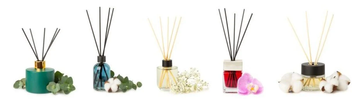 Five assorted reed diffusers in decorative bottles with floral accents placed around them.