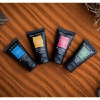 Four black travel-size toiletry tubes with colorful labels arranged on a wooden surface.